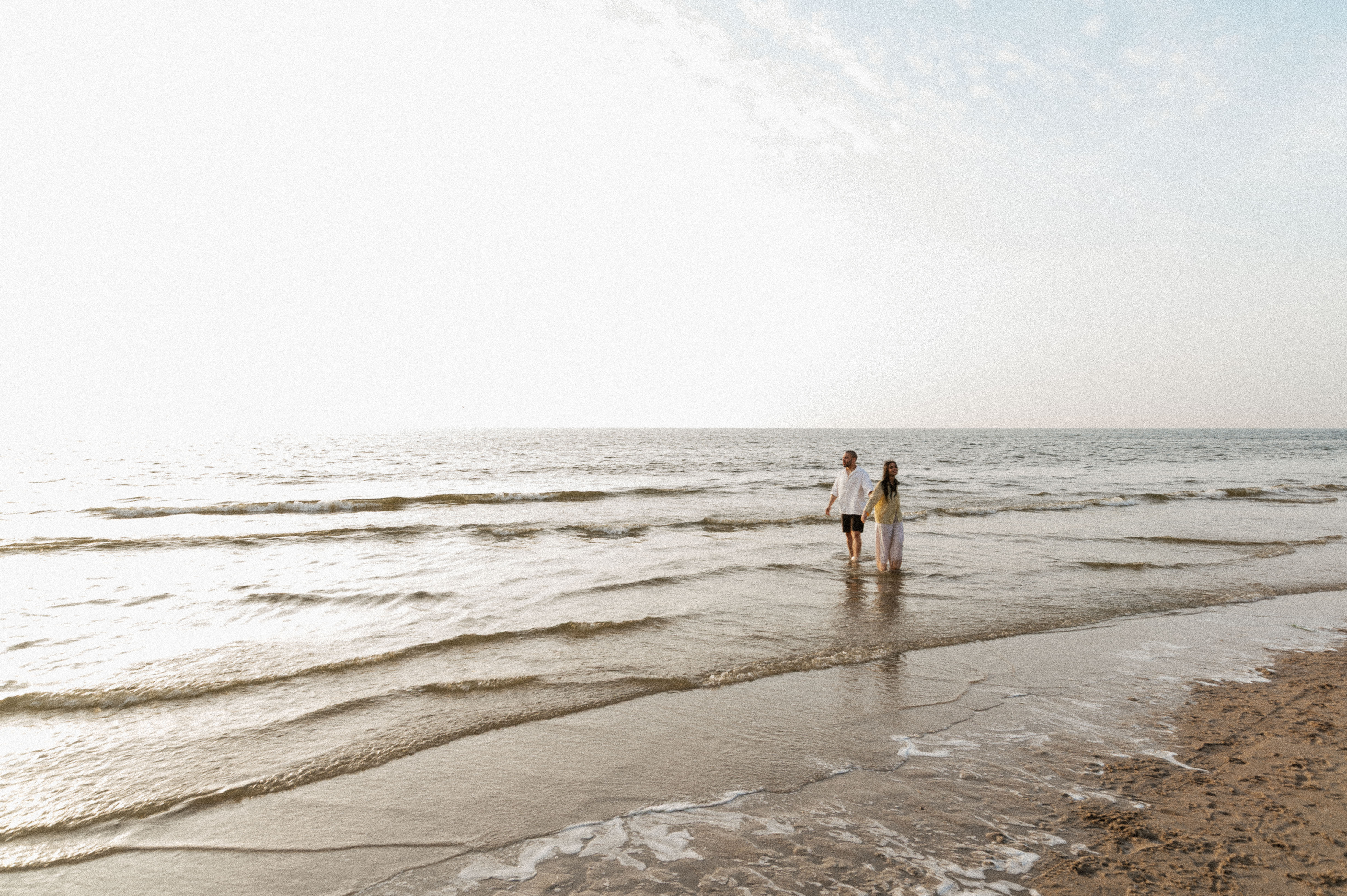 wide shot of couple standing in the ocean at the beach holding hands.