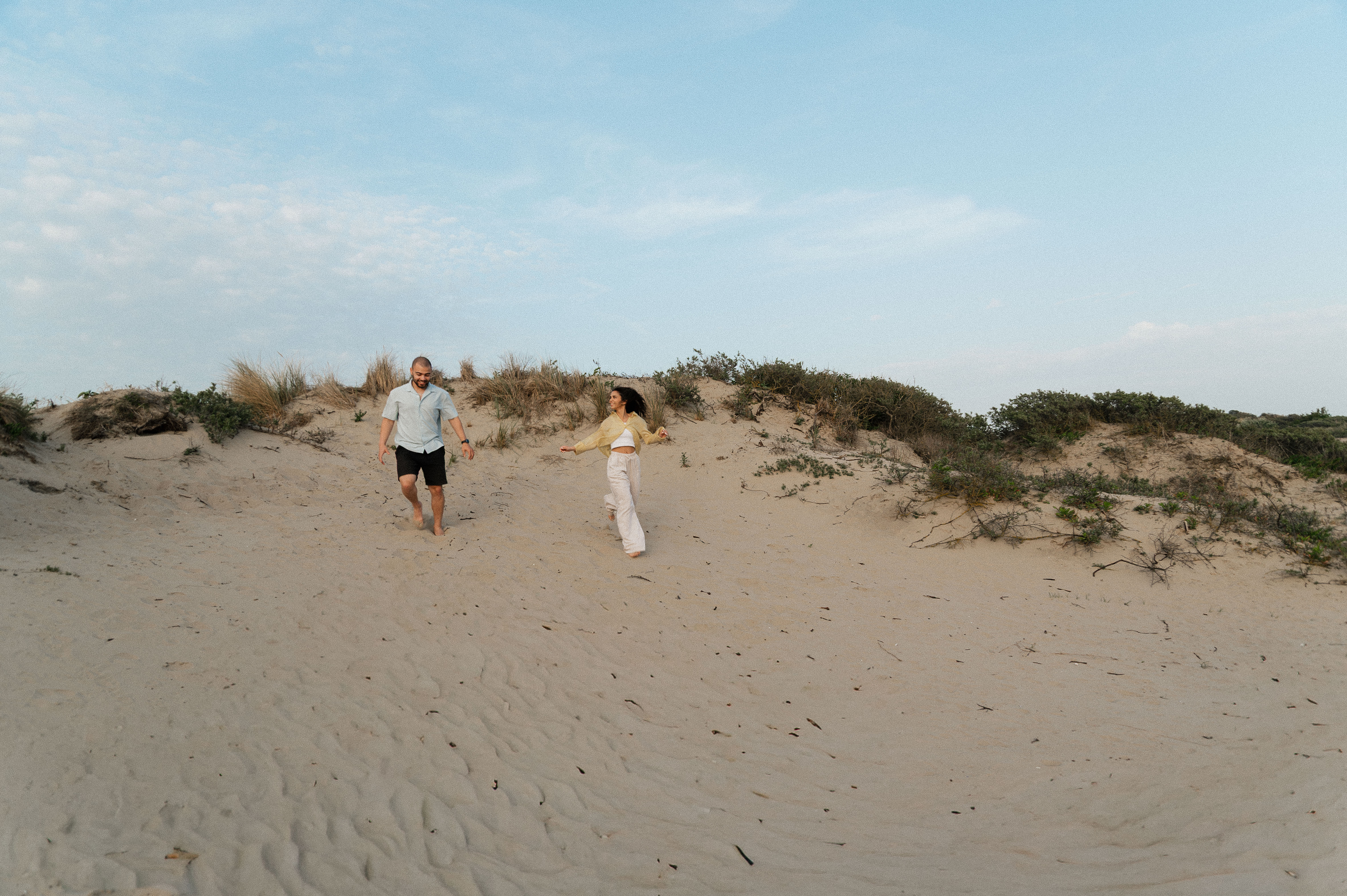 Candid wide shot of couple running down a sand dune next to each other looking at each other.