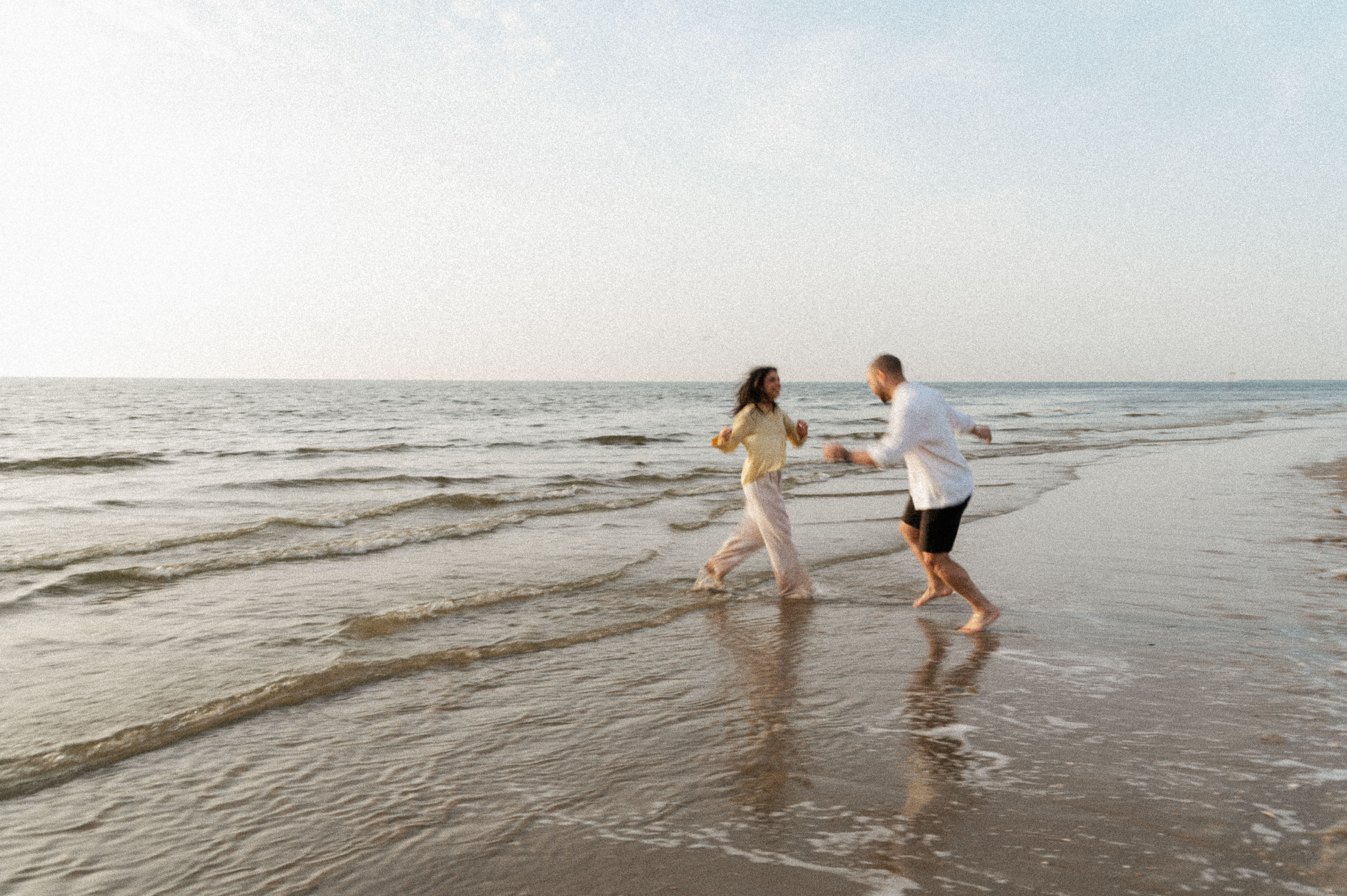 Wide shot of couple playing tag in the shallow water at the beach.