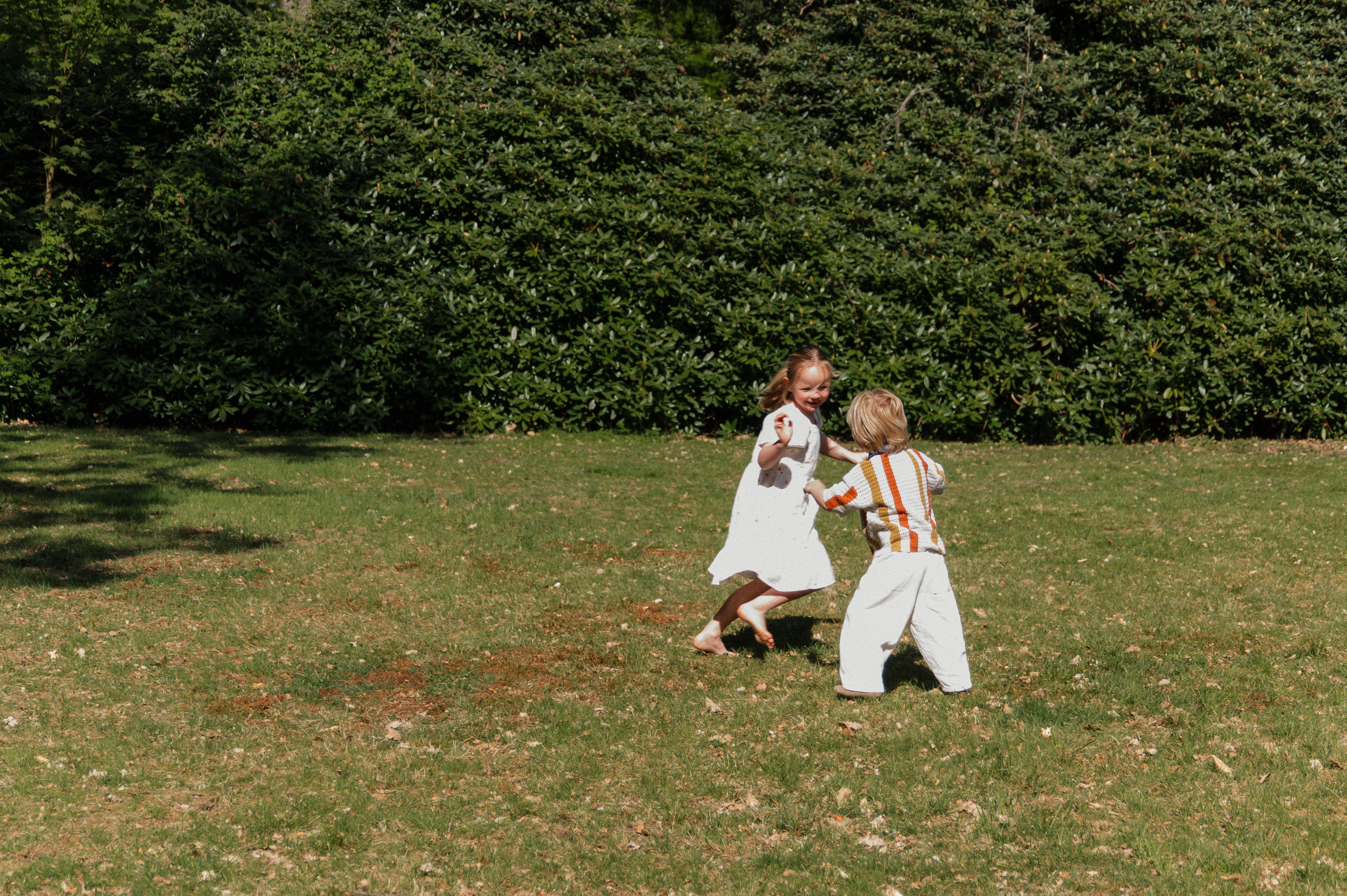Borther and sister running in an open field chasing each other.