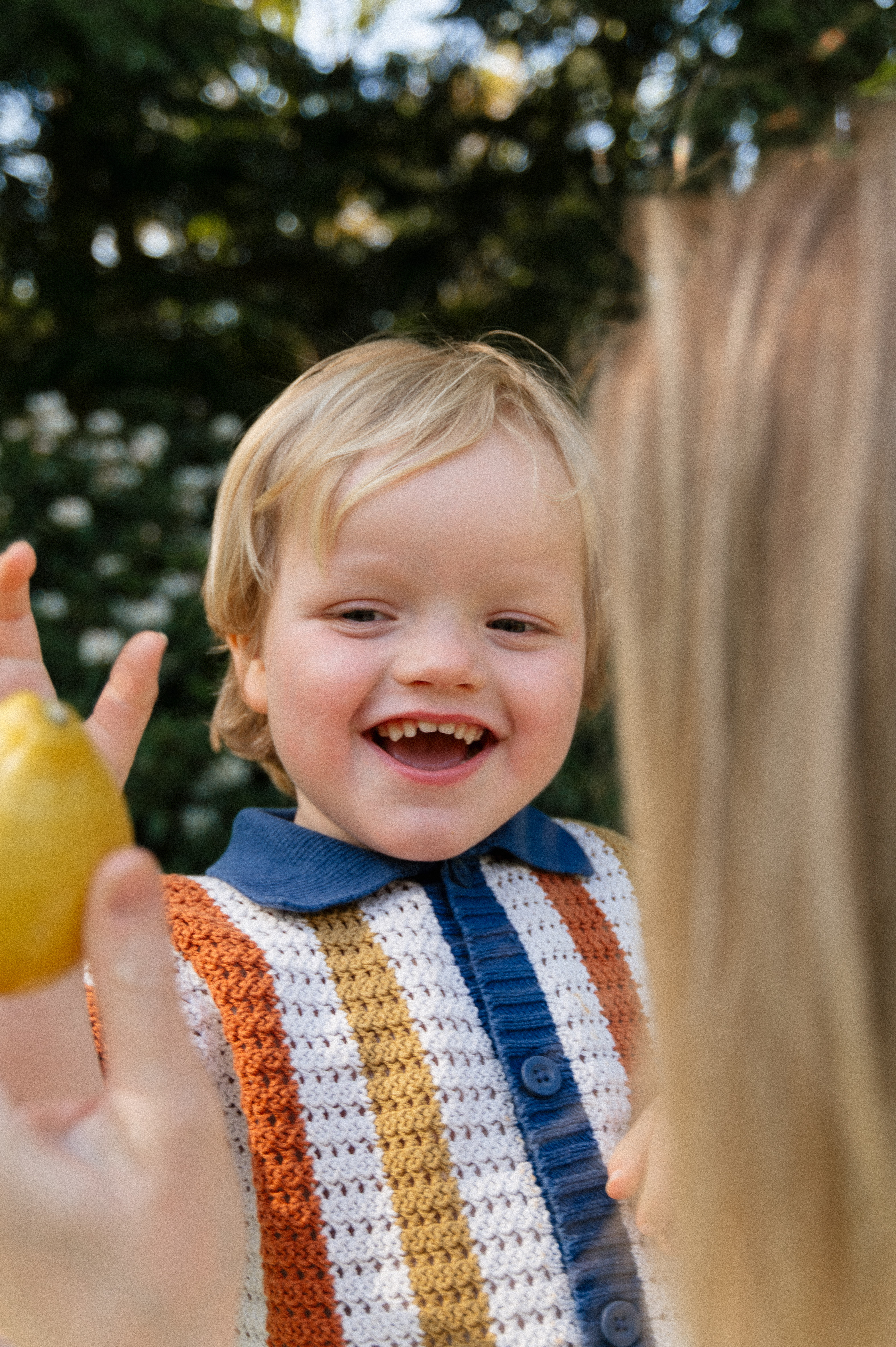 Boy being held by mother on her hip with boy facing camera looking a lemon that mother is holding.