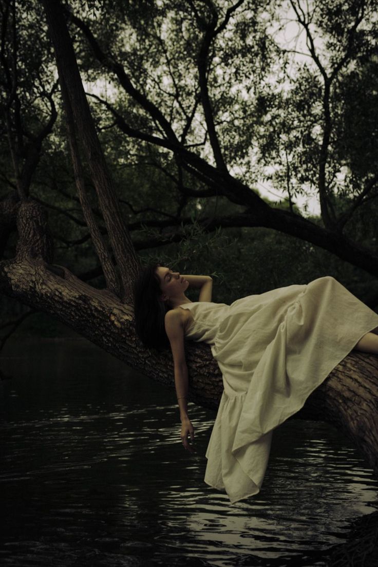 woman lying on tree branch over lake