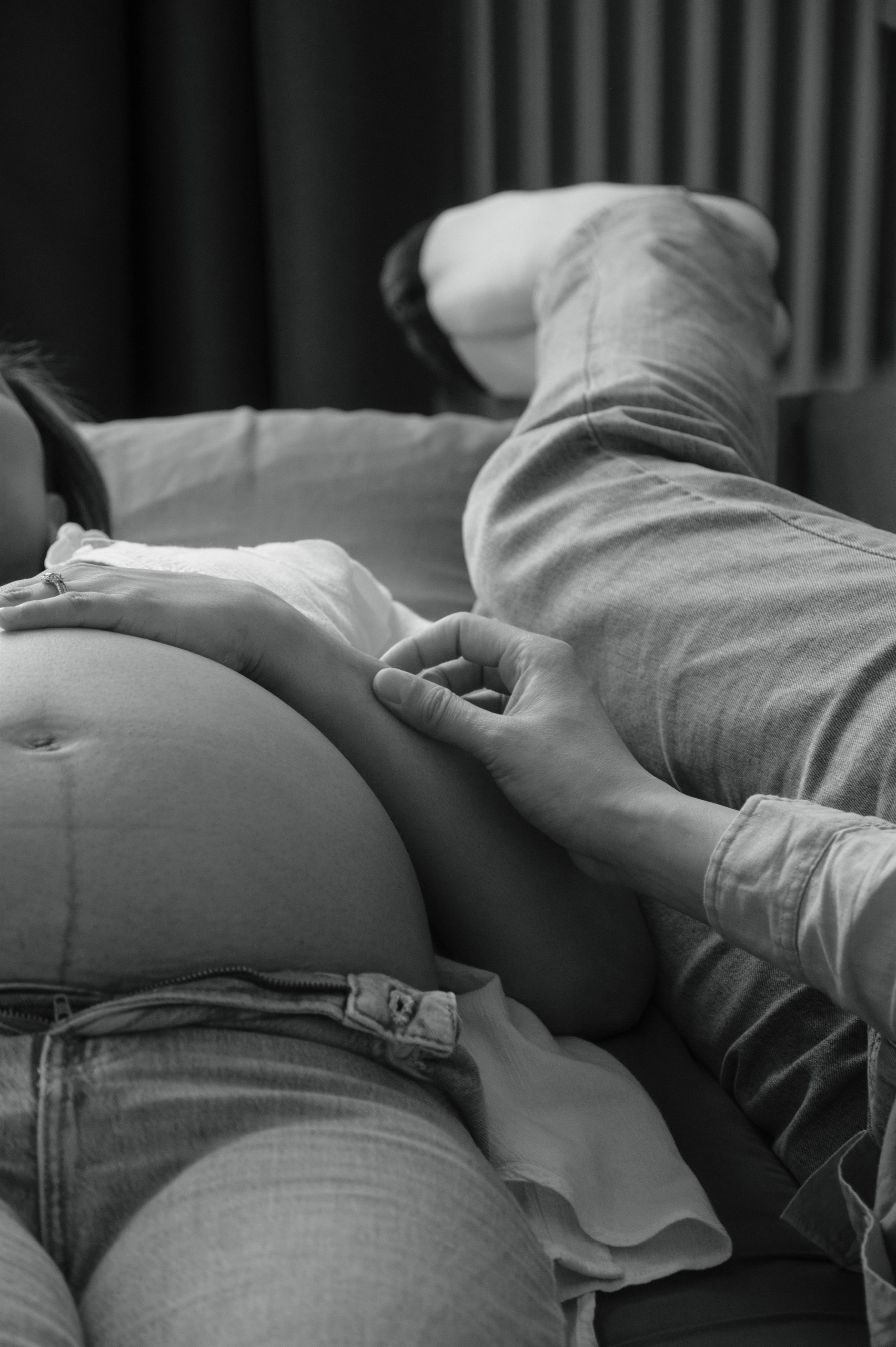 Black-and-white close-up of hands resting on a pregnant belly.