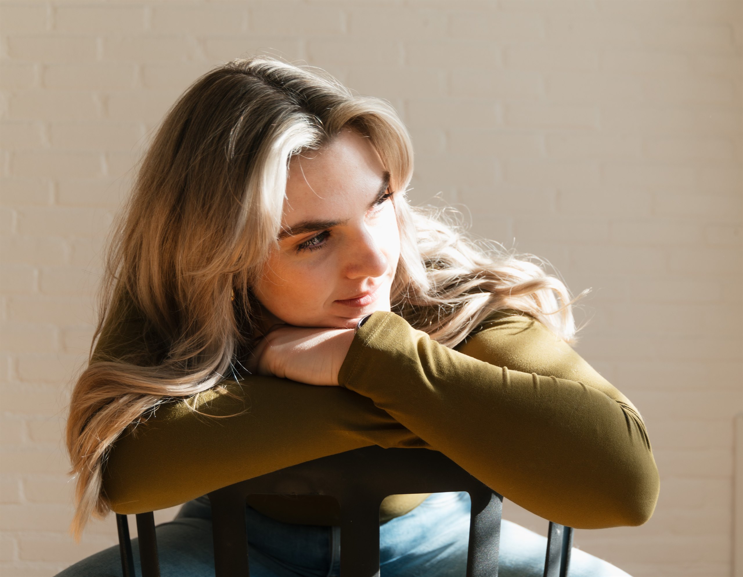 Portrait of a woman resting her arms on a chair in warm sunlight.