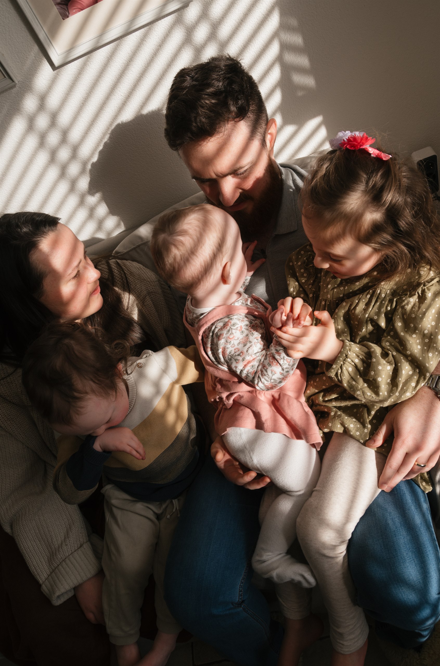 Family gathered around their baby in warm striped window light.