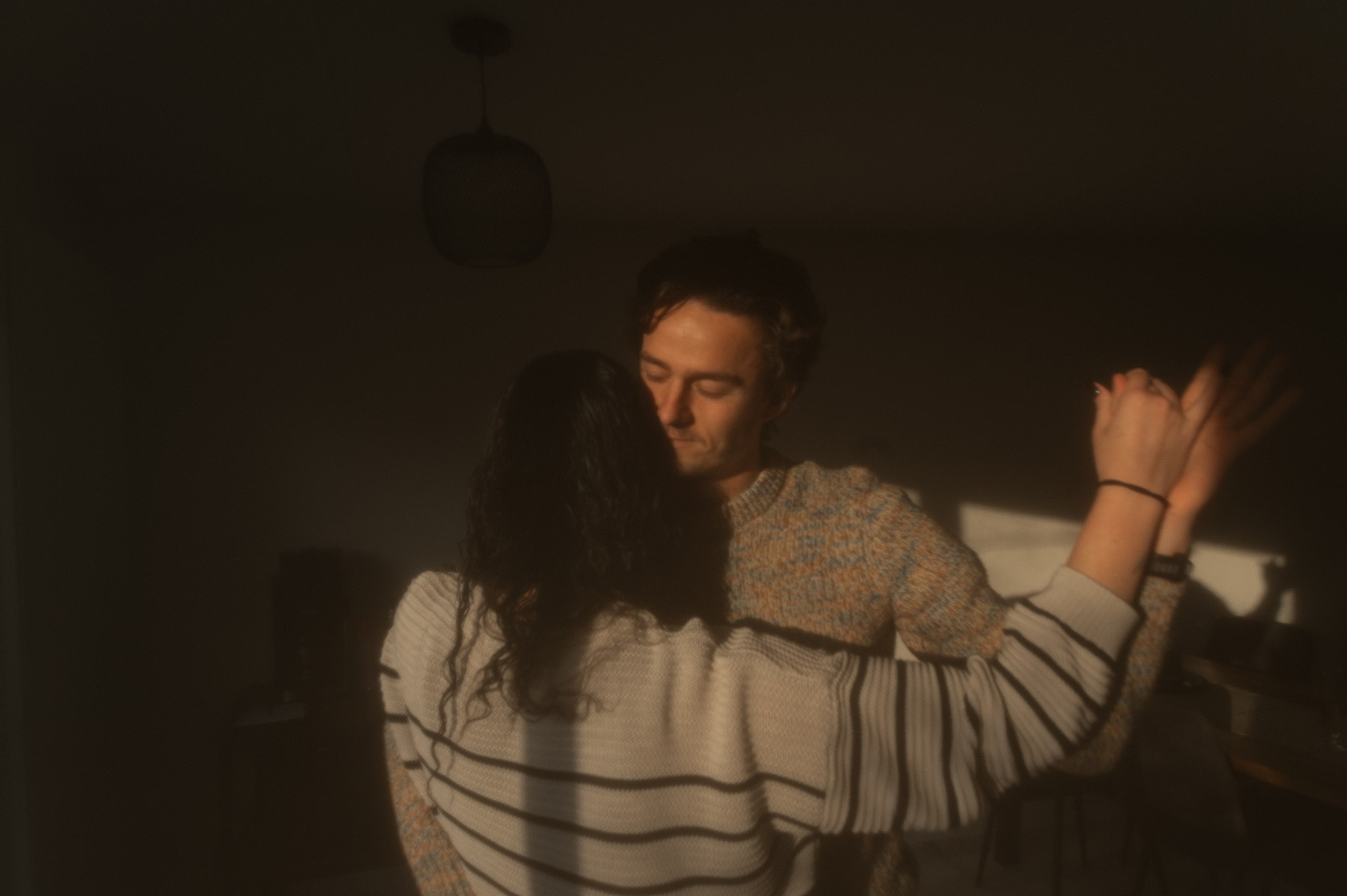 Couple embracing in warm window light at home.