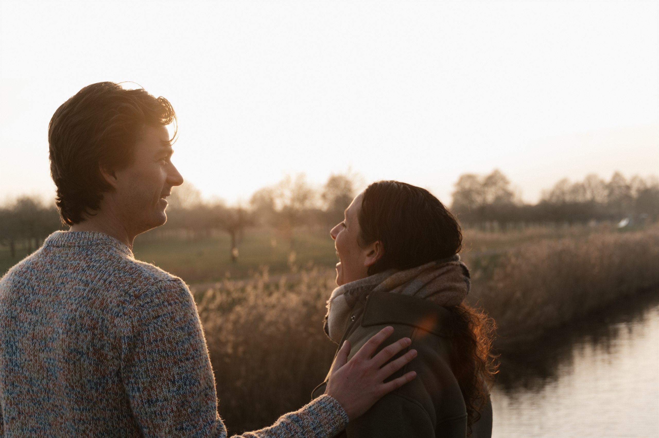 Couple standing together by the water in golden evening light.