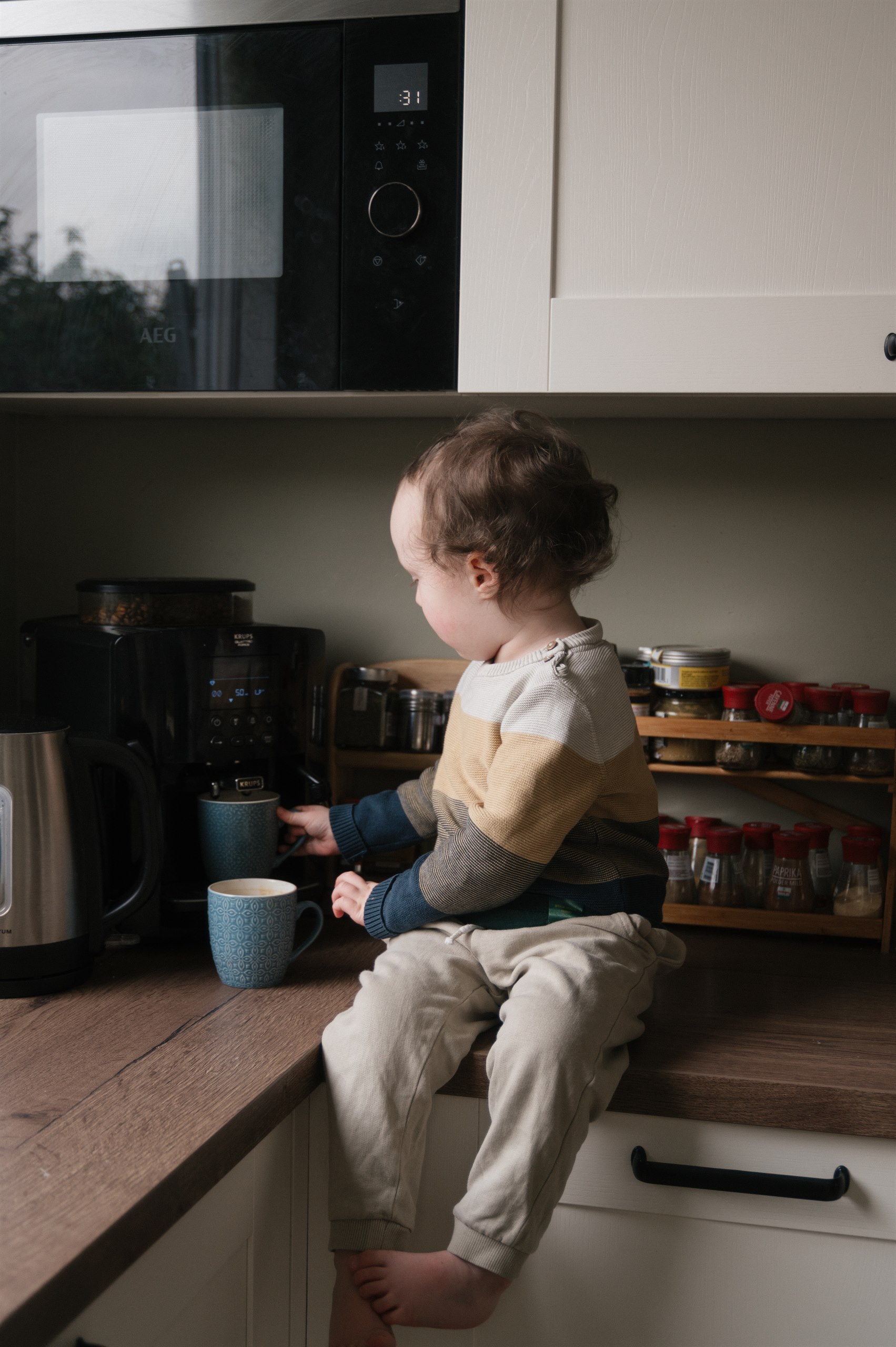 Toddler sitting on a kitchen counter with a mug nearby.