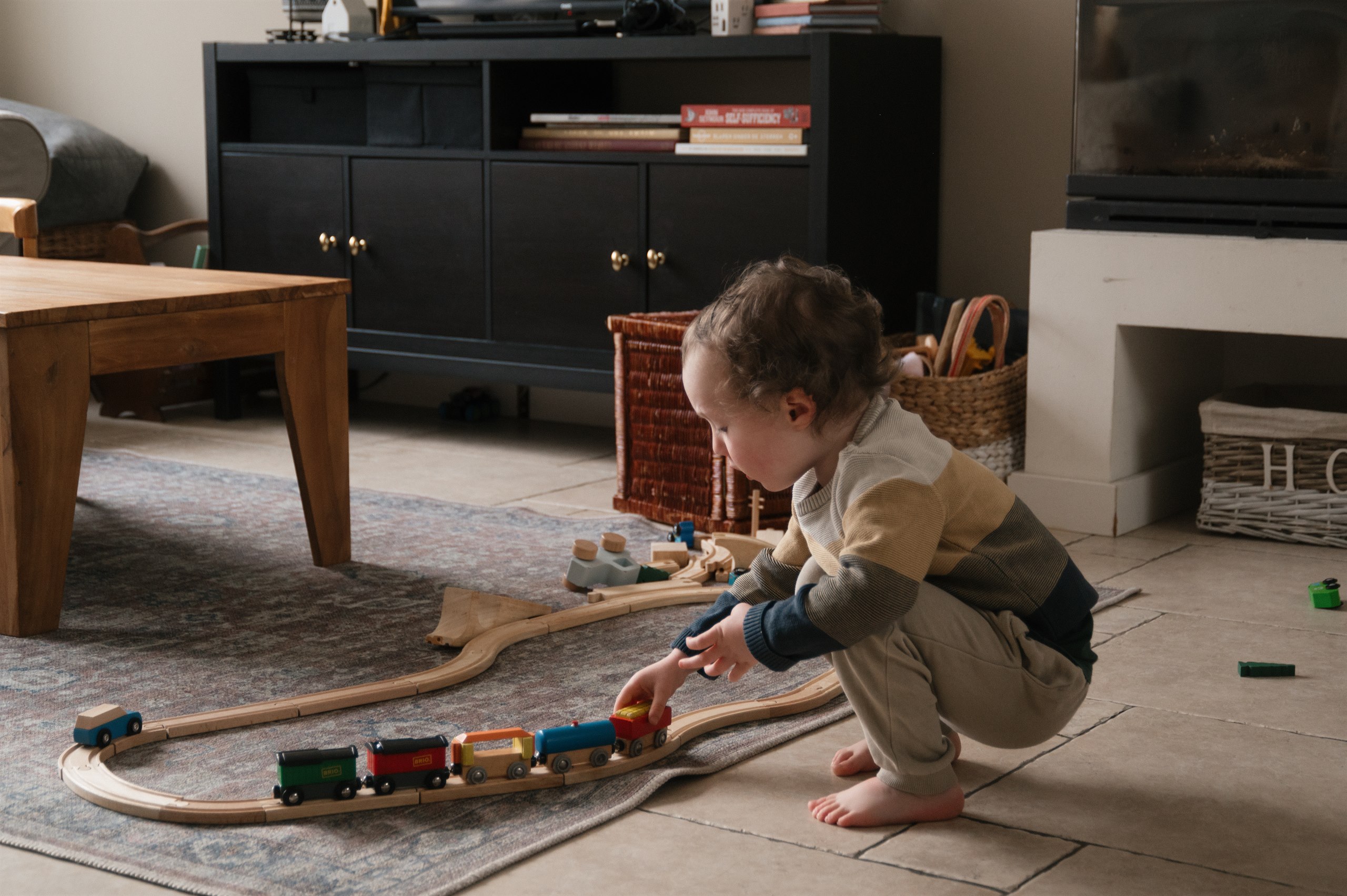 Child playing with a wooden train set on the living room floor.