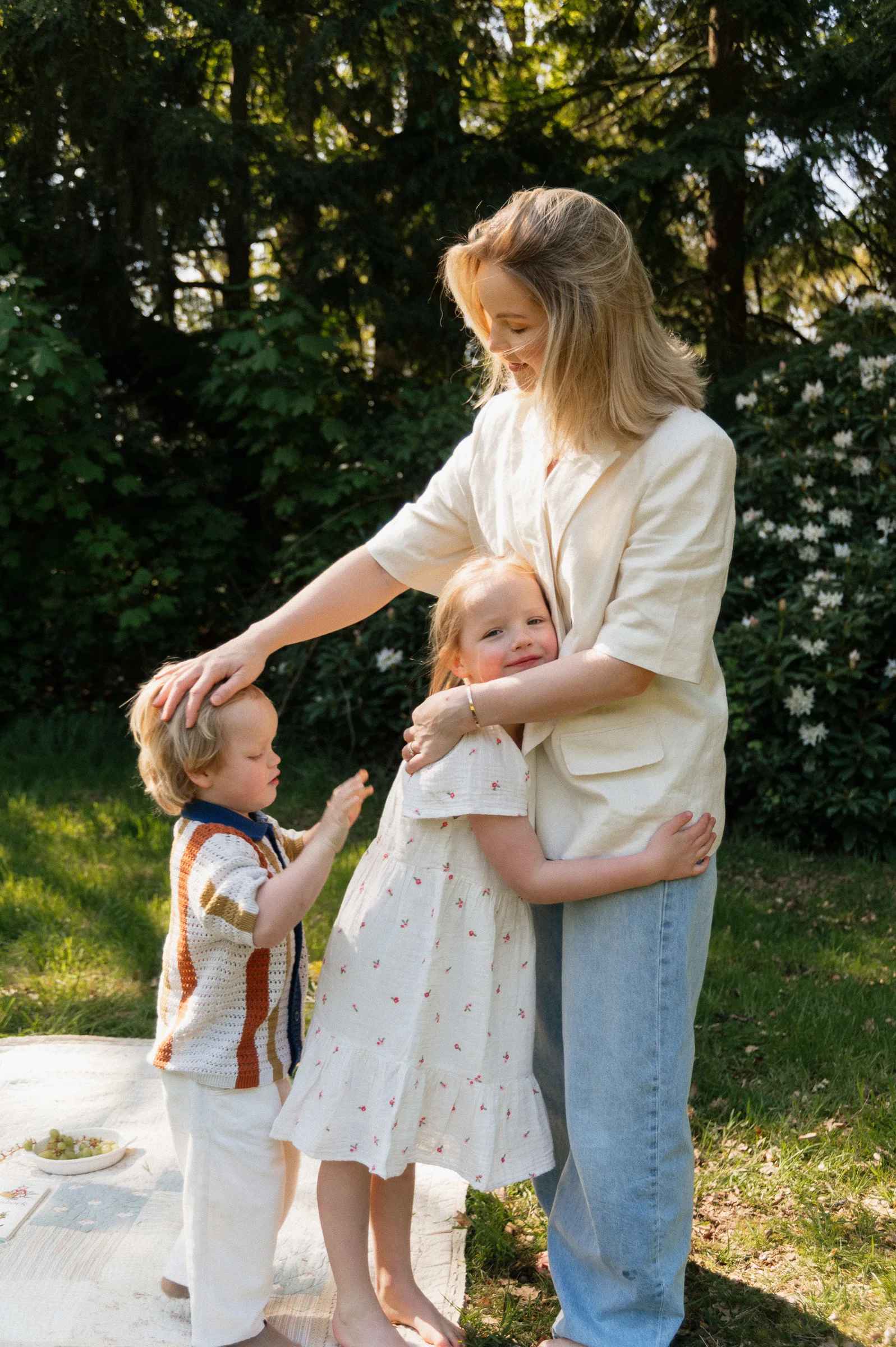 Mother daughter and son standing on picnic blanket embracing each other. Daughter is hugging mom and mom has her hand on son's head.