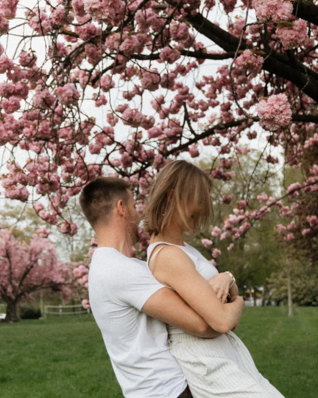 Couple embracing beneath a blooming pink tree.