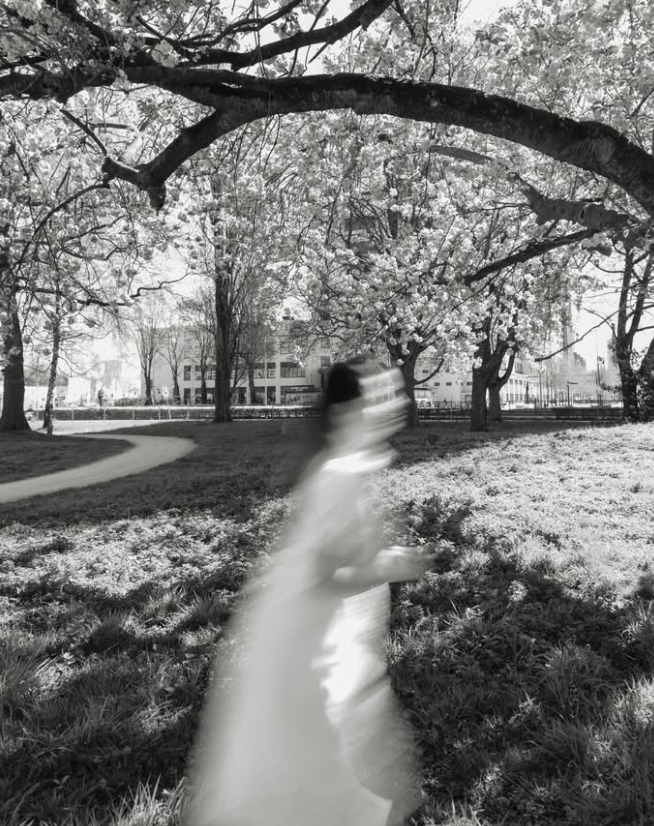 Blurred black-and-white portrait of a woman walking beneath large tree branches.