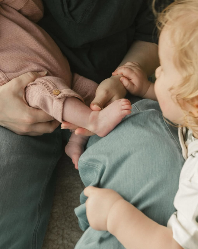 Children touching a newborn's feet while sitting with a parent.