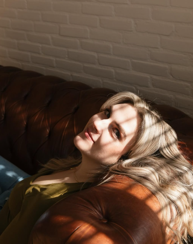Portrait of a woman reclining on a leather sofa in striped sunlight.