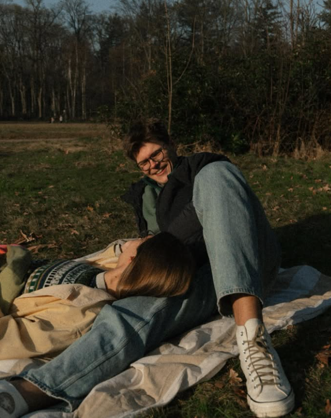 Couple cuddling on a picnic blanket outdoors.