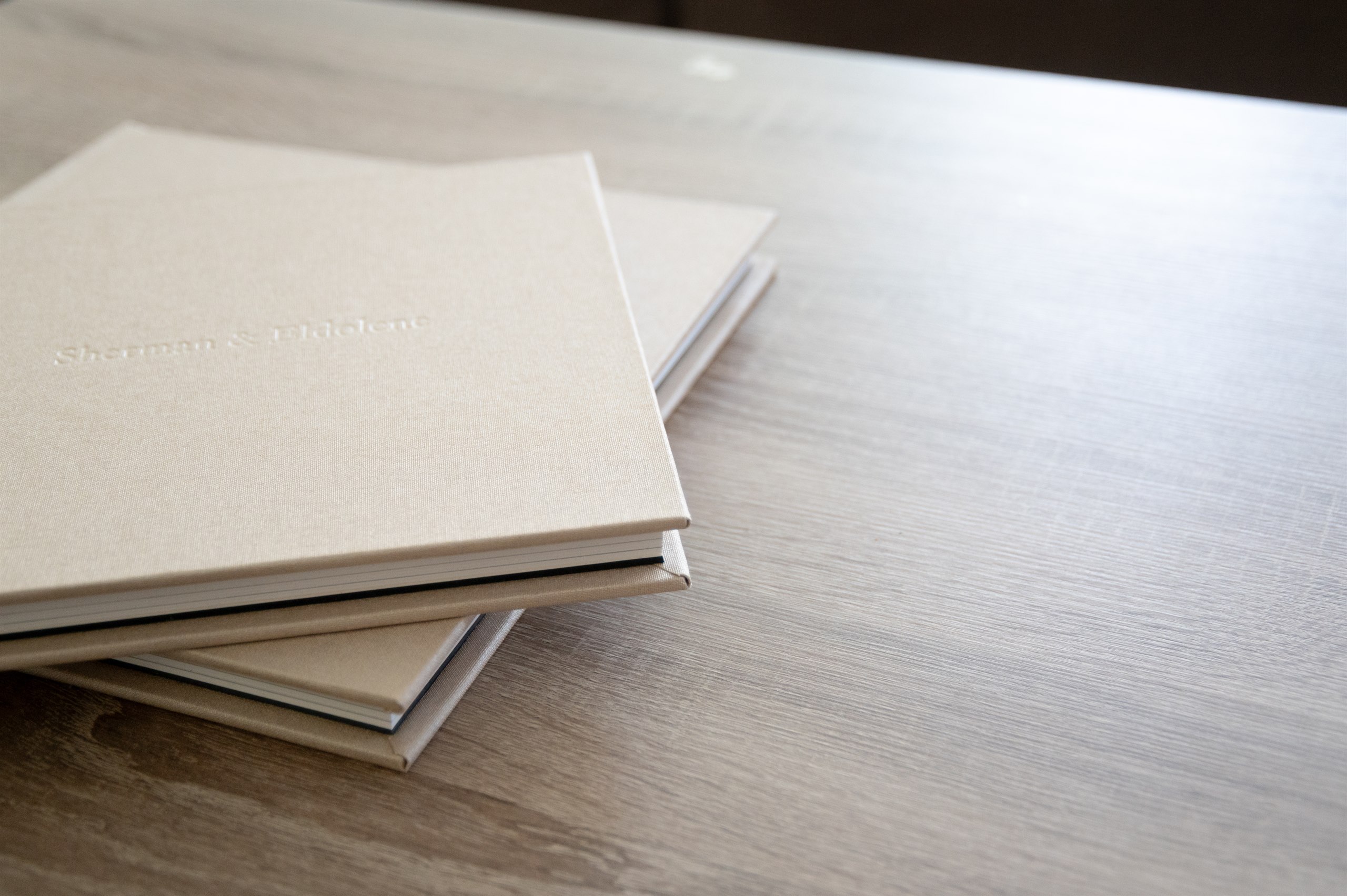 Stack of linen photo albums on a wooden table.