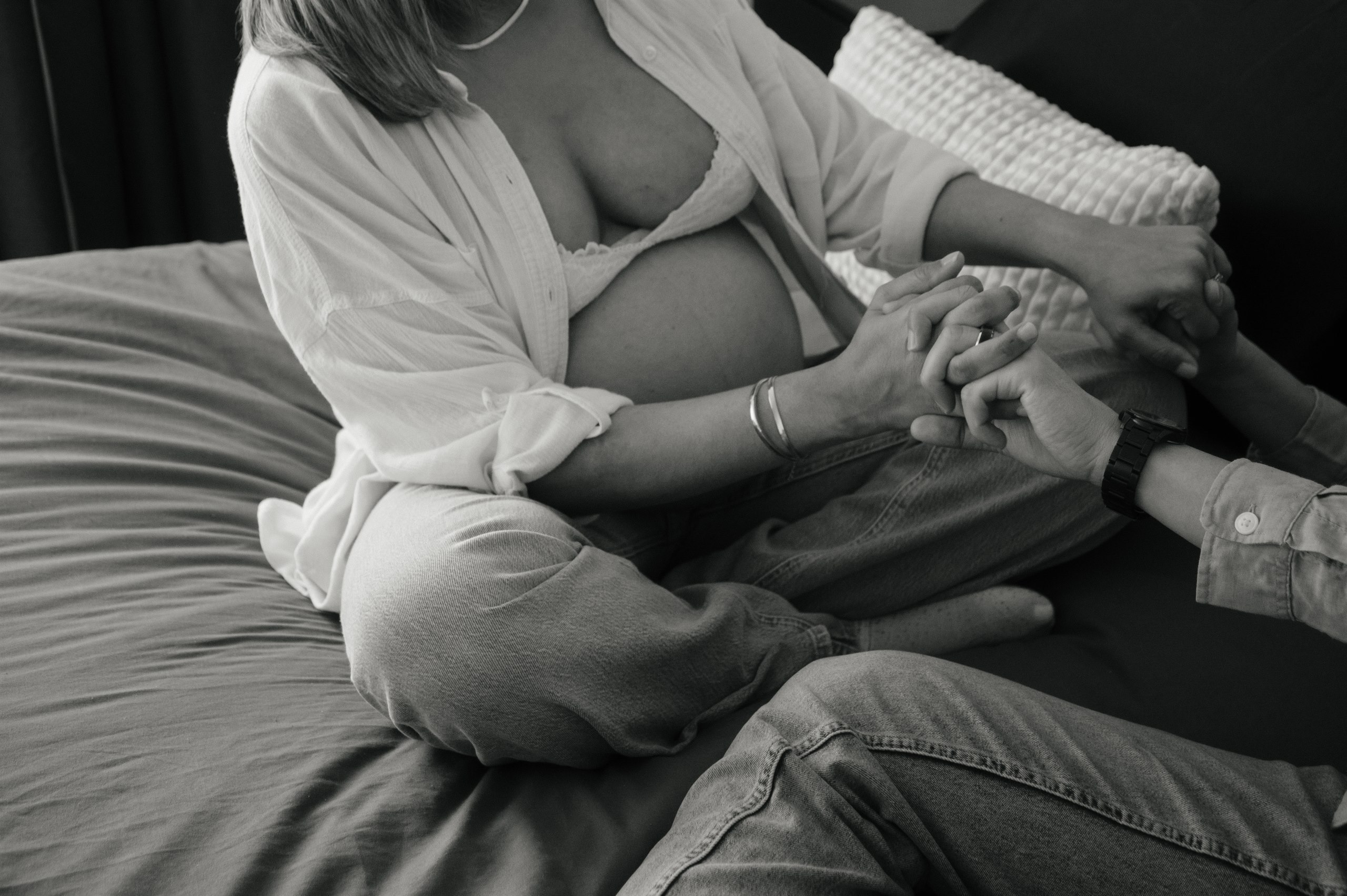 Expectant mother sitting on a bed while holding hands with her partner.