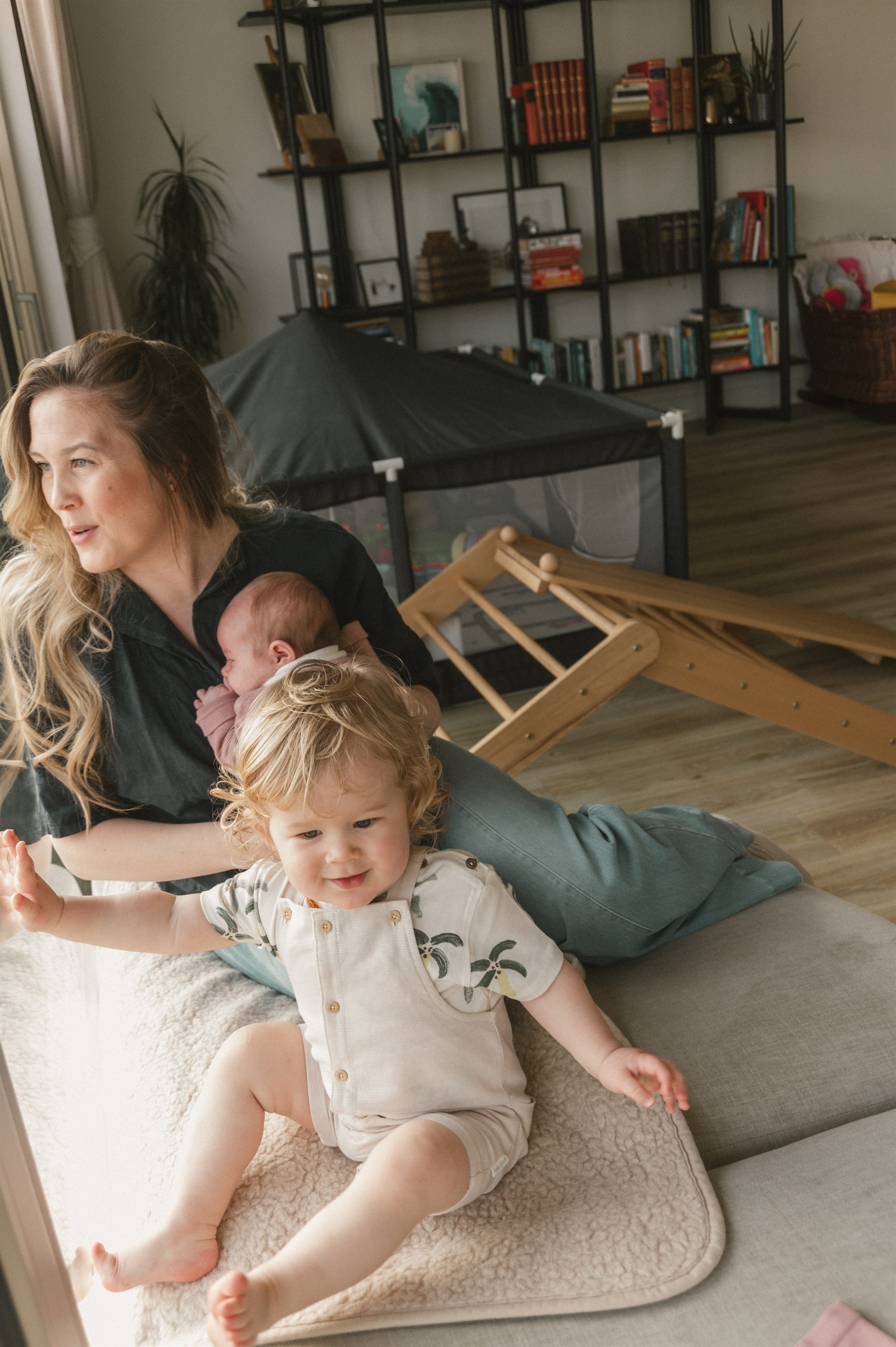 Mother sitting on the floor with her baby and toddler in soft window light.