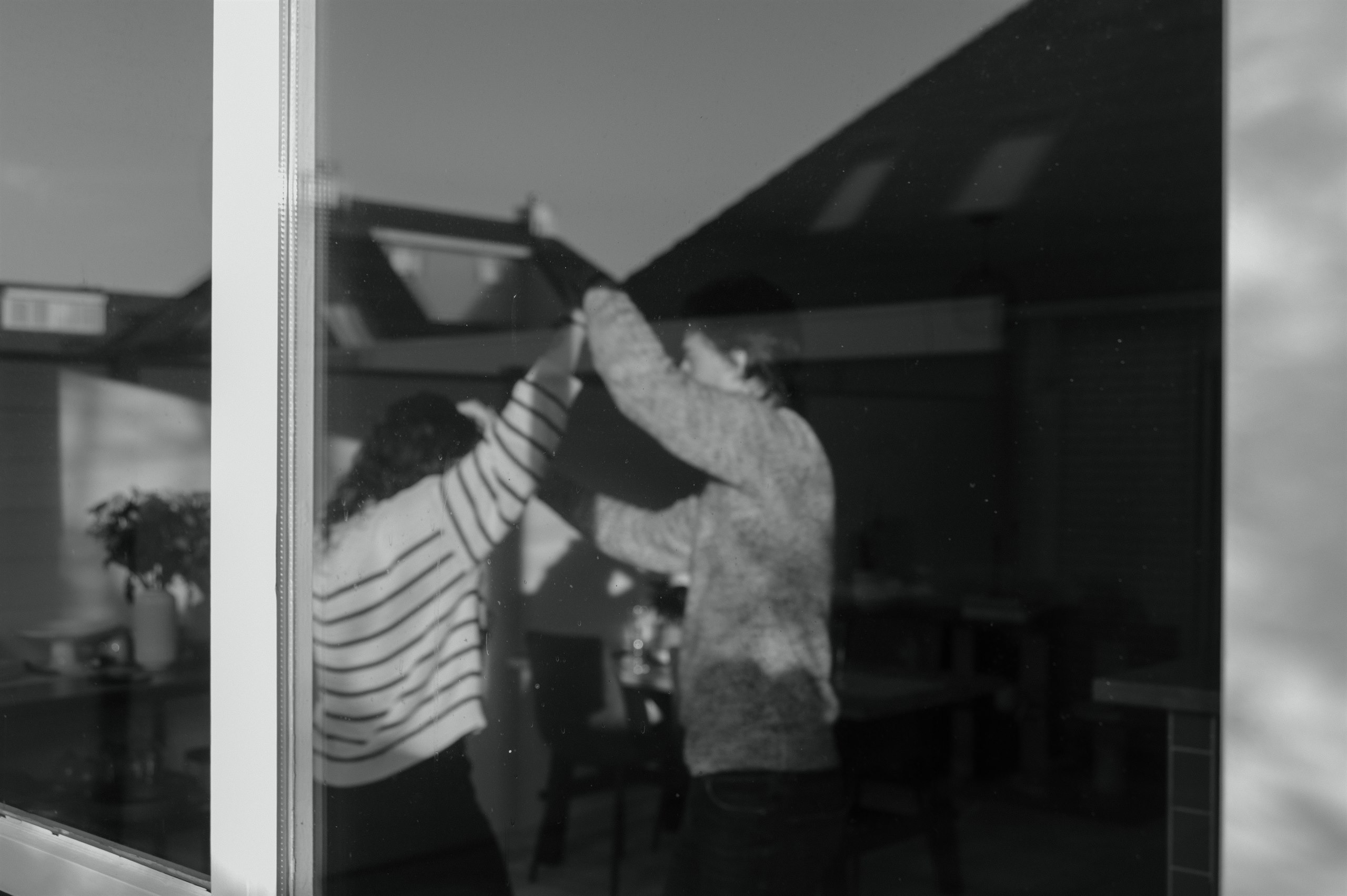 Black-and-white reflection of a parent and child at a glass door.