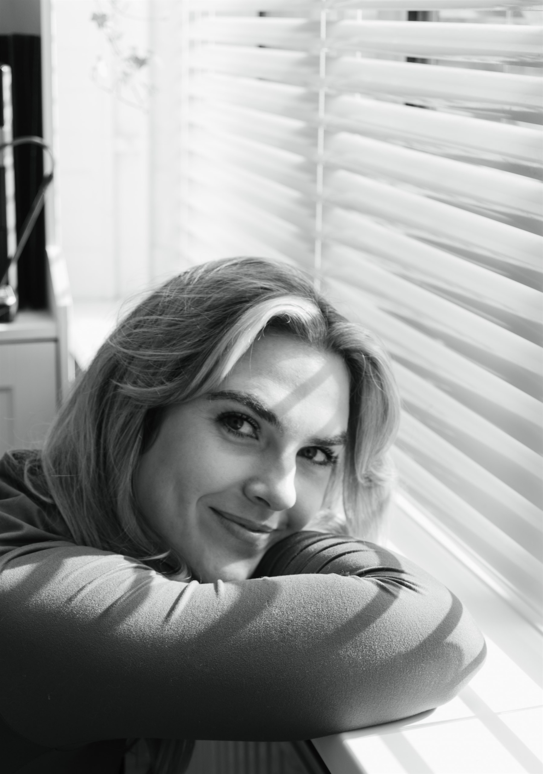 Black-and-white portrait of a woman leaning by a window.