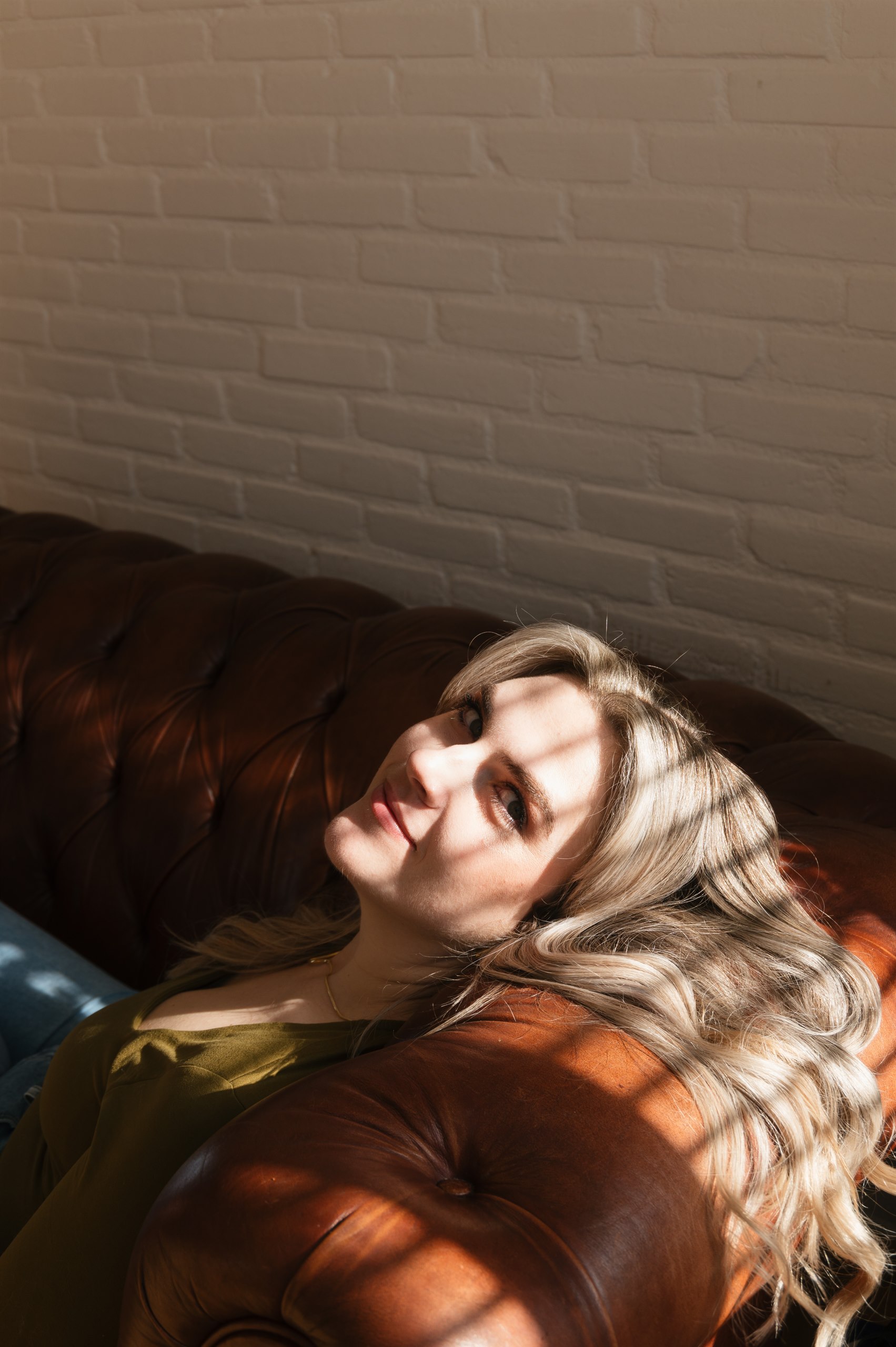 Portrait of a woman reclining on a leather sofa in warm sunlight.